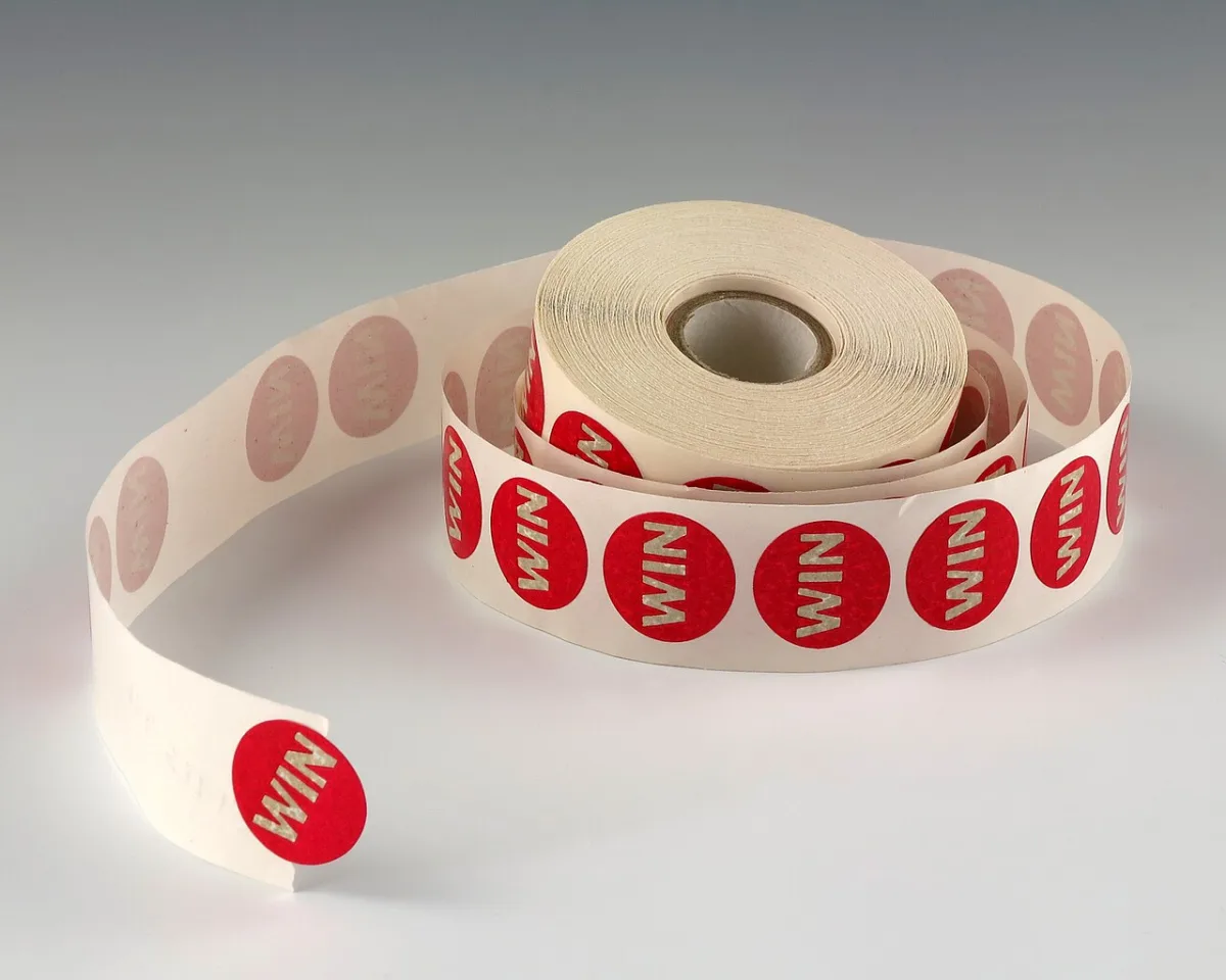 Rol met ronde stickers waarop het woord WIN gedrukt staat, uitgerold op een lichte ondergrond.